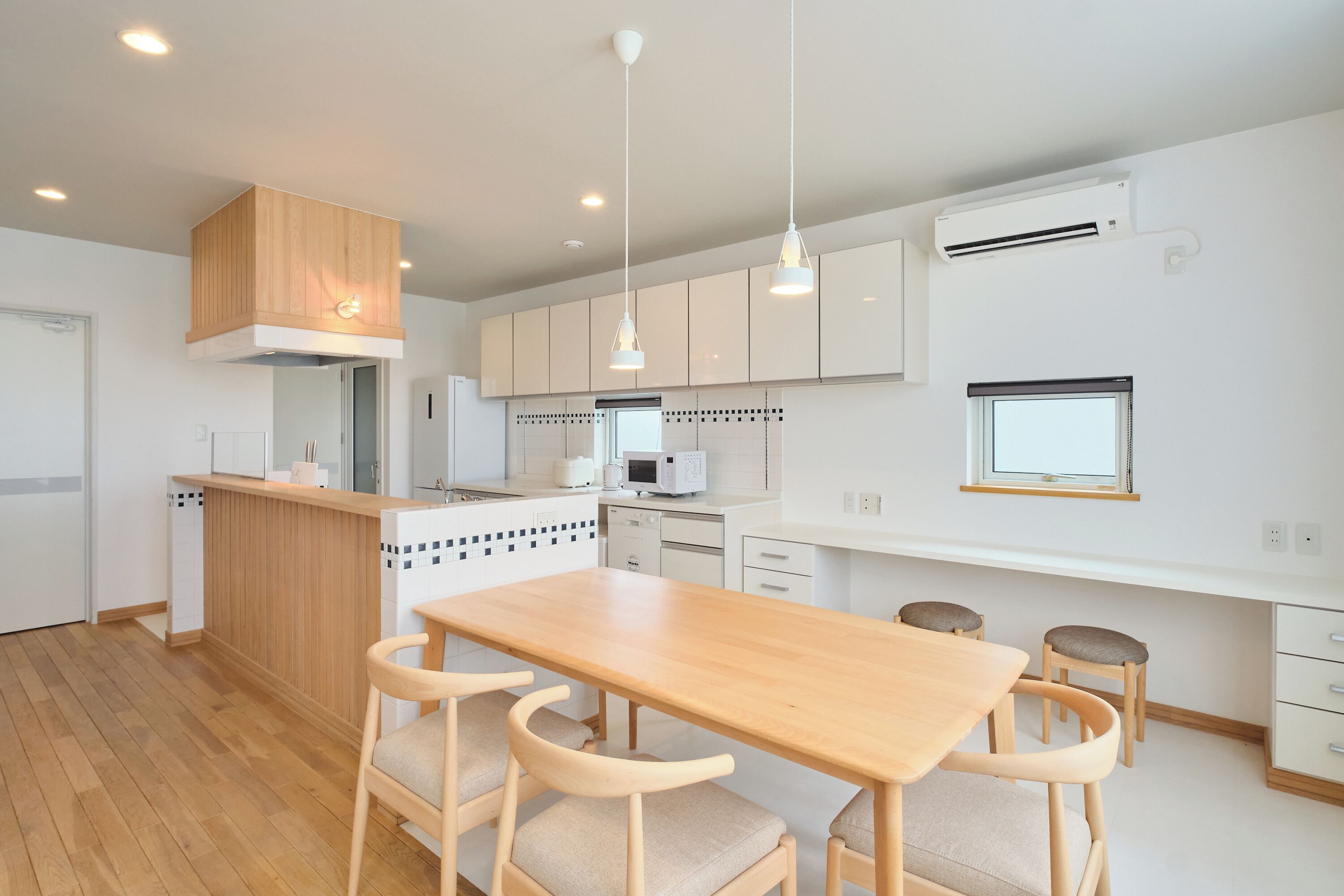 A modern kitchen with wooden cabinetry, a central island, pendant lighting, and a dining area with a wooden table and chairs.