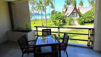 A balcony with a table and chairs, overlooking a beach and a house with a unique roof design.