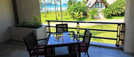 Un balcon avec une table et des chaises, donnant sur une plage et une maison dont le toit présente un design original.
