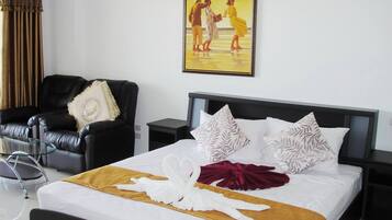 A hotel room with a bed, a chair, a nightstand, and a painting on the wall.