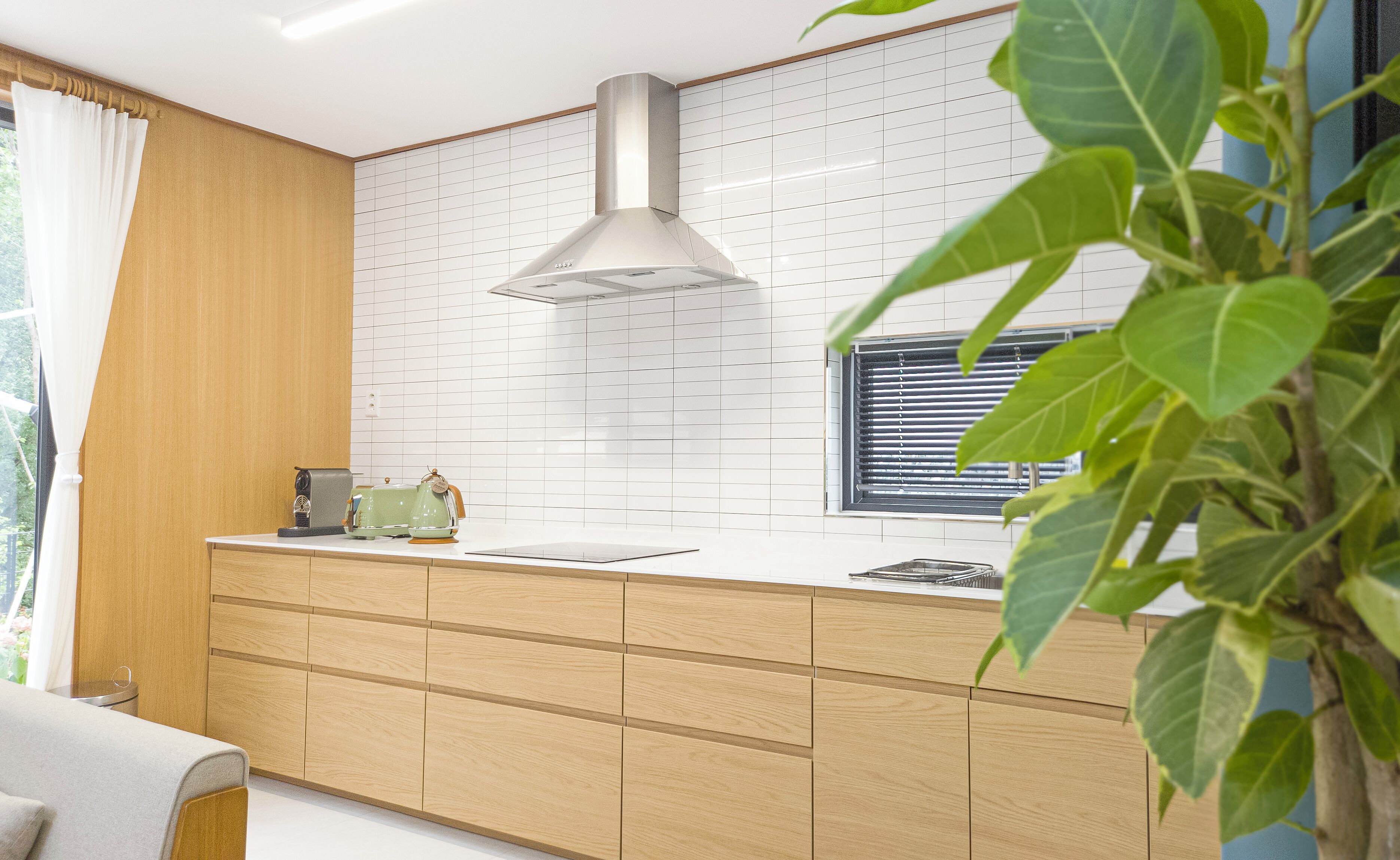 A modern kitchen with wooden cabinetry, a stainless steel range hood, and a window with blinds.