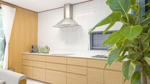 A modern kitchen with wooden cabinetry, a stainless steel range hood, and a window with blinds.