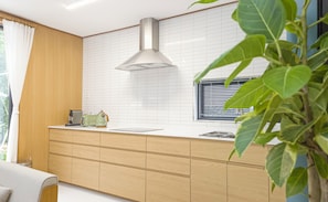 A modern kitchen with wooden cabinetry, a stainless steel range hood, and a window with blinds.