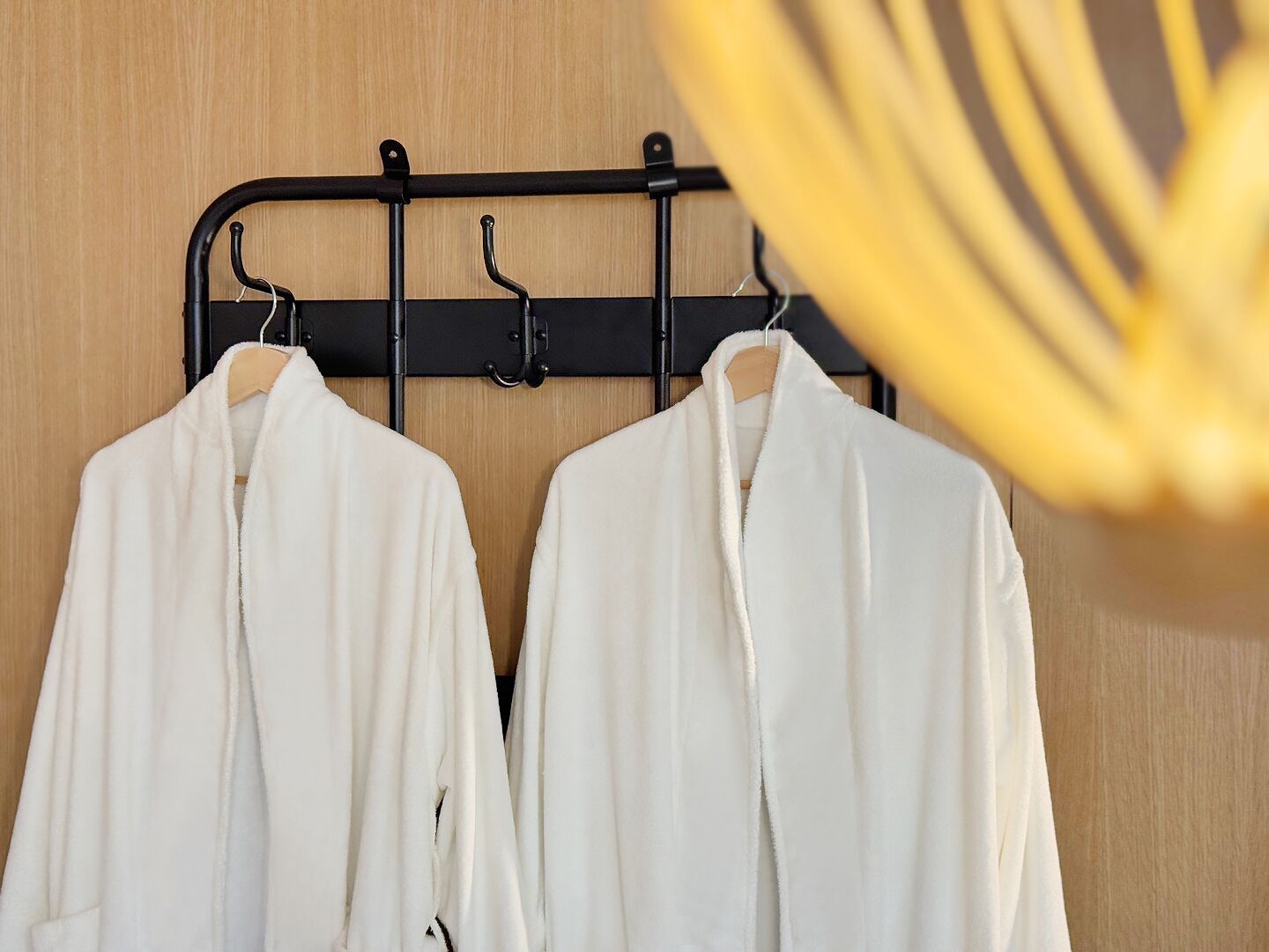 Two white robes hanging on a black rack against a wooden wall.
