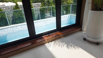 Habitación con un gran ventanal con vista a una piscina, piso de madera y un pilar blanco.