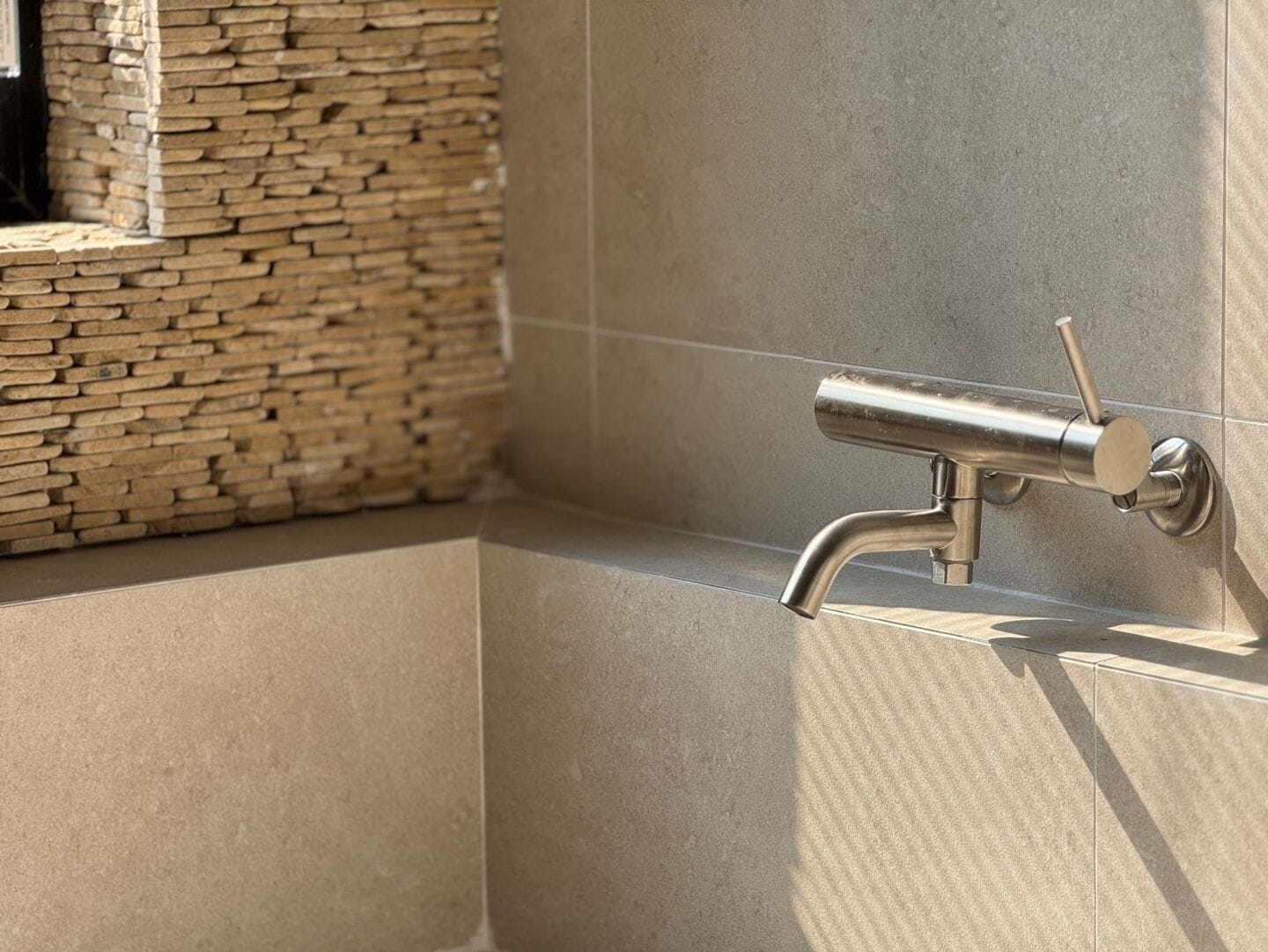 A modern bathroom with a stone wall and a metallic faucet.