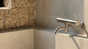 A modern bathroom with a stone wall and a metallic faucet.