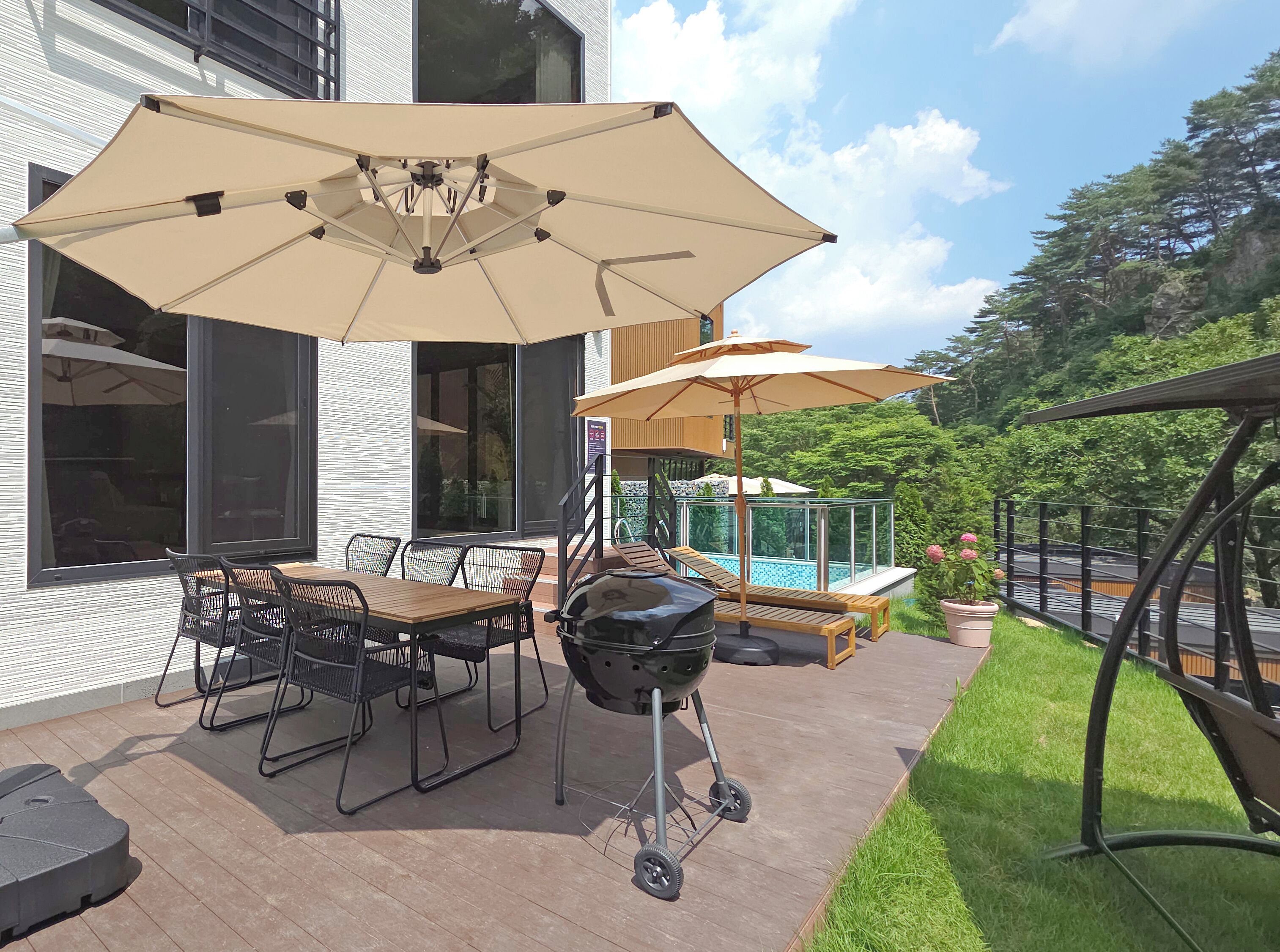 An outdoor patio with a dining table, chairs, a grill, and umbrellas.