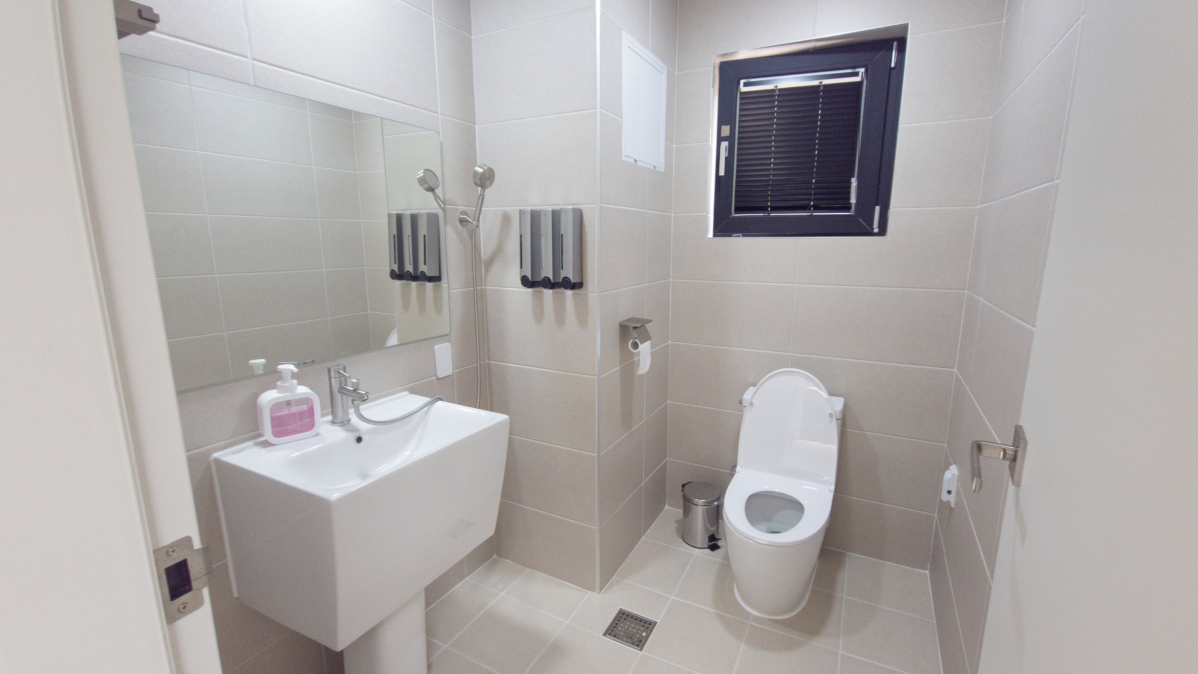 A bathroom with a white sink, mirror, toilet, and a window with blinds.