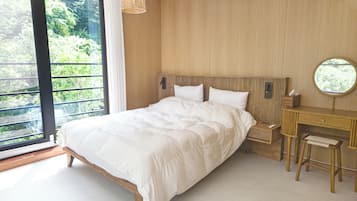 A bedroom with a large bed, a wooden headboard, a bedside table, a mirror, and a view of greenery outside.