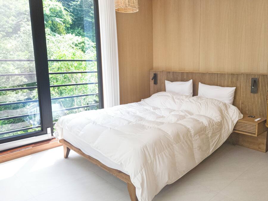 Una camera da letto con un letto grande, una testiera in legno, un comodino, uno specchio e vista sul verde.