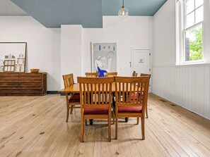 En matplats med ett träbord och stolar, en tavla på väggen och ett fönster med utsikt över grönområden.