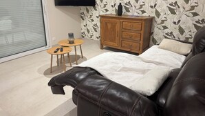 En moderne stue med en lædersofa, et træskab, et fladskærms TV og et rundt bord med en fjernbetjening.