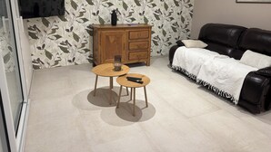 En stue med sofa, et træskab, to runde borde og et fjernsyn ophængt på væggen.