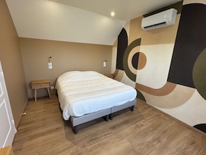 A bedroom with a bed, a bedside table, an air conditioning unit, and a wall with a geometric design.
