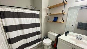 Un baño con cortina de ducha a rayas, un inodoro, un lavabo blanco y estantes de madera sobre el inodoro.