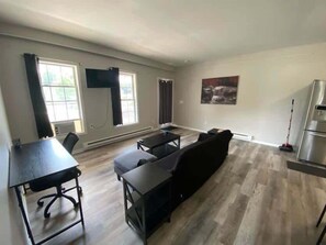 A spacious living area with a sofa, a dining table, and a TV mounted on the wall.