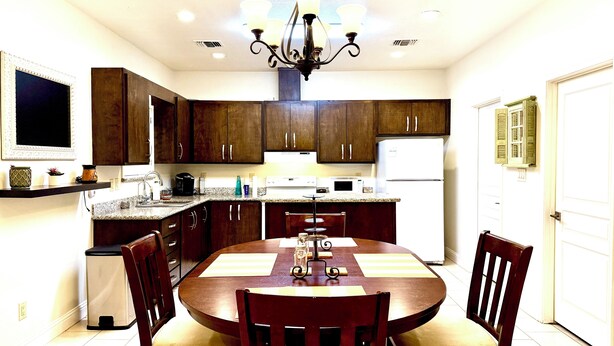 A kitchen with dark wooden cabinets, a white refrigerator, a dining table with chairs, and a chandelier. - CasaDeCarrion: 30+Day Extended Corporate Stay Fully Furnished 3bd/2.5ba (San Antonio)