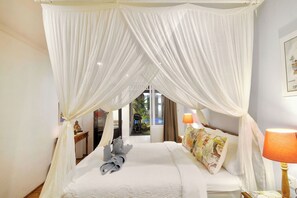 A hotel room with a bed, a bedside table, a lamp, and a view of the outside. - Selasih Beach House (Badung)