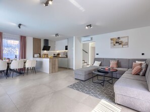 A modern living room with a grey sofa, a dining area with chairs, a kitchen with a central island, and a staircase leading to an upper level. - Vacation home LaLuMa by Interhome (Pula)