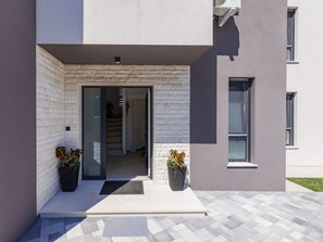 A modern building entrance with a glass door, a small outdoor seating area, and potted plants. - Vacation home LaLuMa by Interhome (Pula)