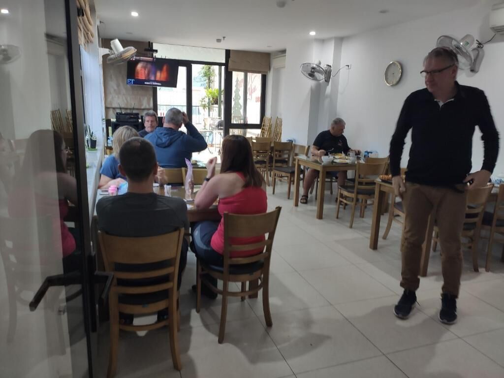 Un espace repas comprenant plusieurs tables et chaises, un téléviseur fixé au mur et une horloge également fixée au mur.