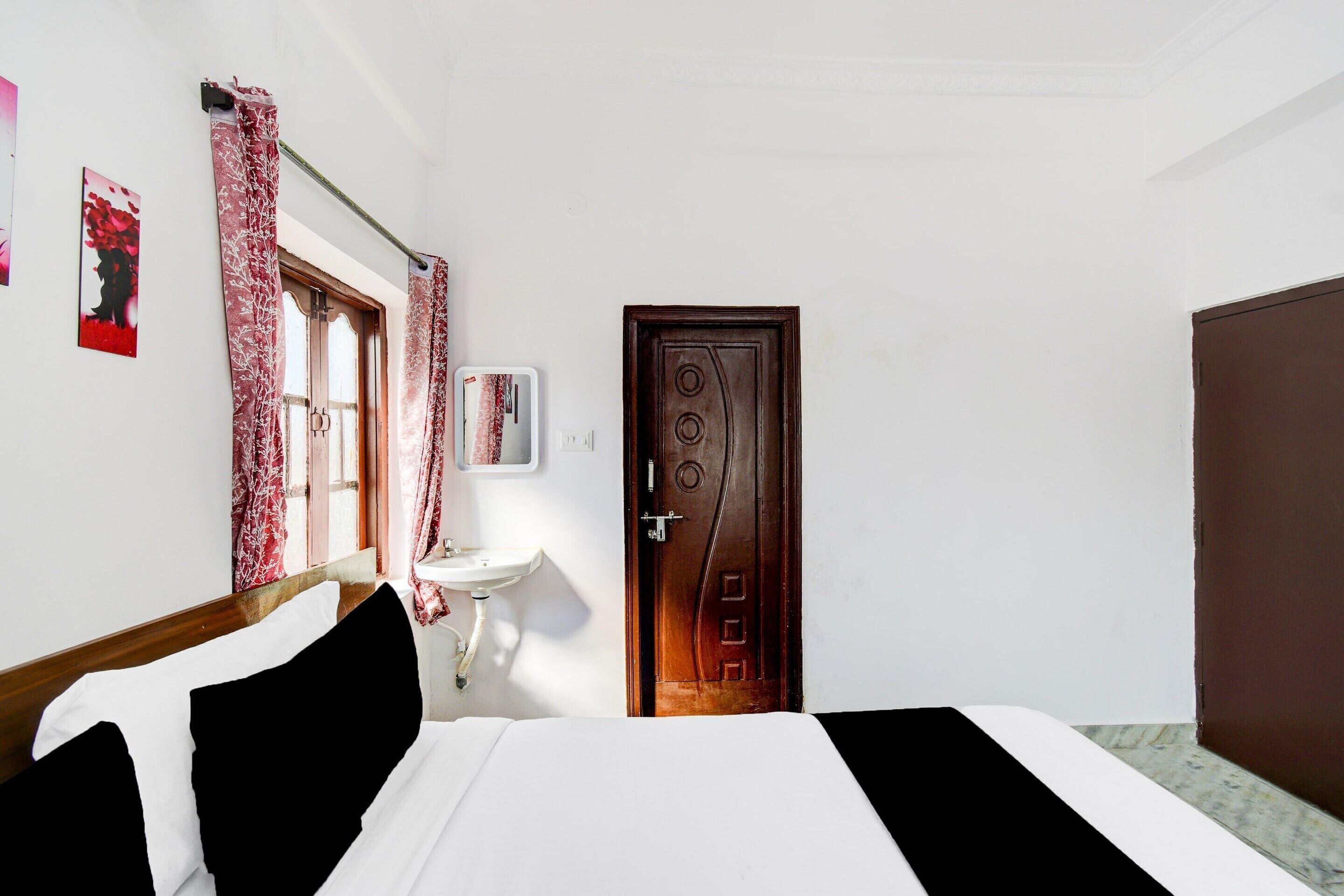 Une chambre à coucher avec un lit, une table de chevet, un miroir, une fenêtre avec des rideaux et une porte.