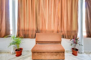 A room with a cushioned bench, two potted plants, and a curtain backdrop.