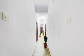 A corridor with white walls, a marble floor, and potted plants.