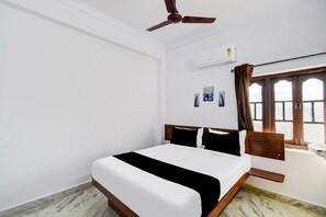 A hotel room with a bed, a ceiling fan, an air conditioning unit, a window with curtains, and a wall-mounted artwork. - Classic Hotel a Qube (Hyderabad)