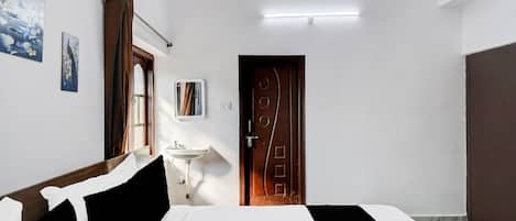 A hotel room with a bed, a bedside table, a mirror, a window with curtains, a wall-mounted air conditioner, and a door.