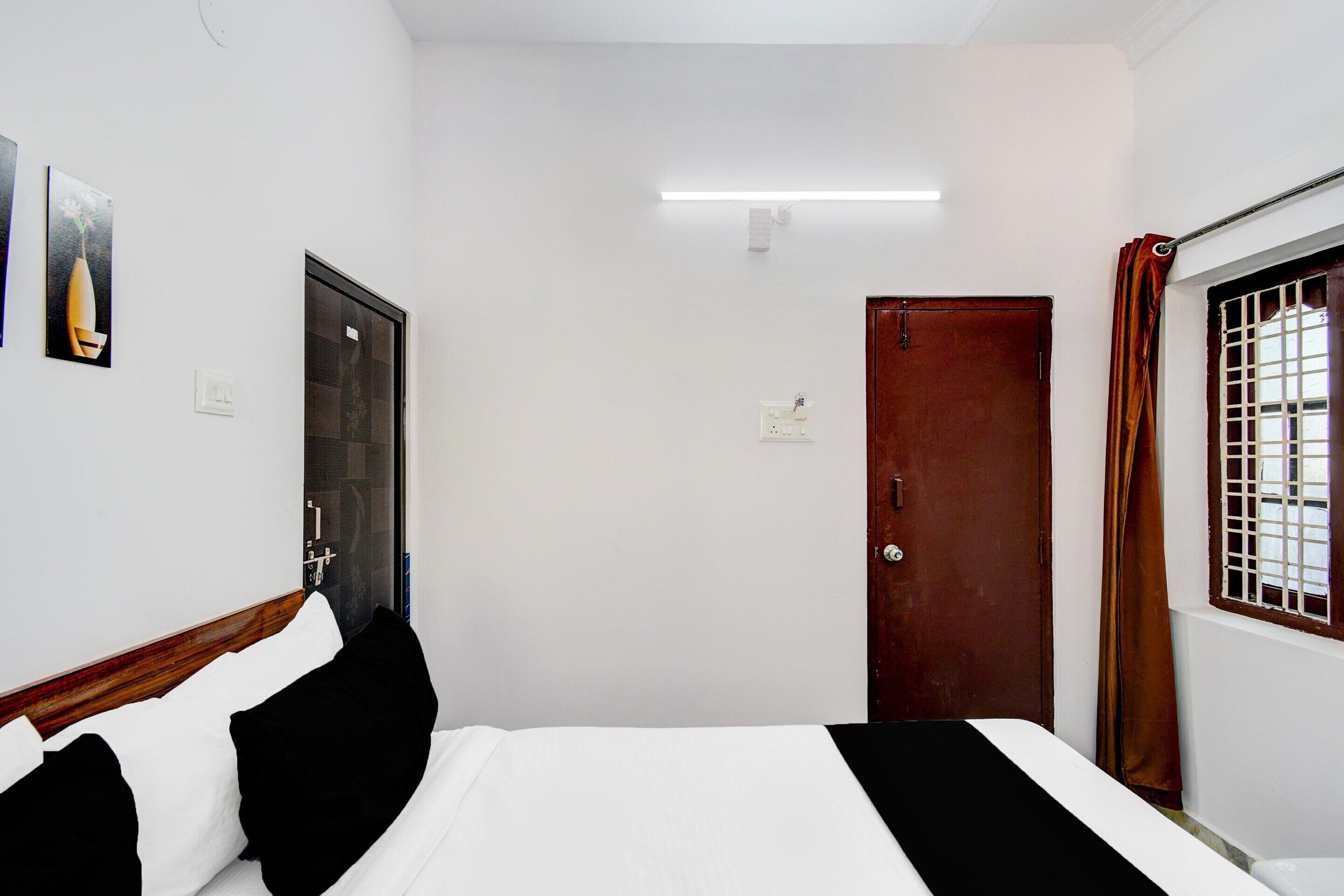 A hotel room with a bed, a door, a window with bars, and a wall-mounted light fixture.
