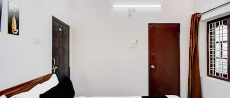 A hotel room with a bed, a door, a window with bars, and a wall-mounted light fixture.