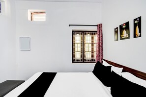 Ett hotellrum med en säng, ett fönster med galler, en väggmonterad lampa och en liten luftkonditioneringsanläggning.