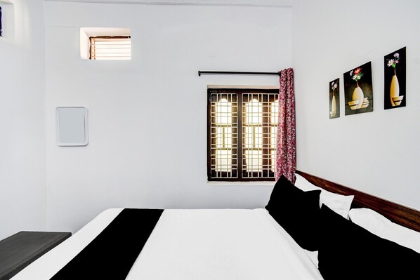 A hotel room with a bed, a window with bars, a wall-mounted light, and a small air conditioning unit.