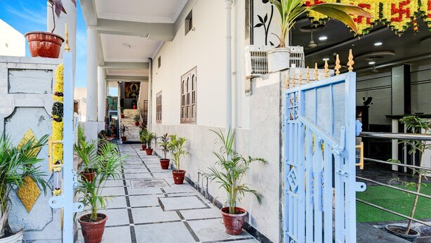 Un pasillo con piso de baldosas, plantas en macetas y una puerta azul que da a un edificio.