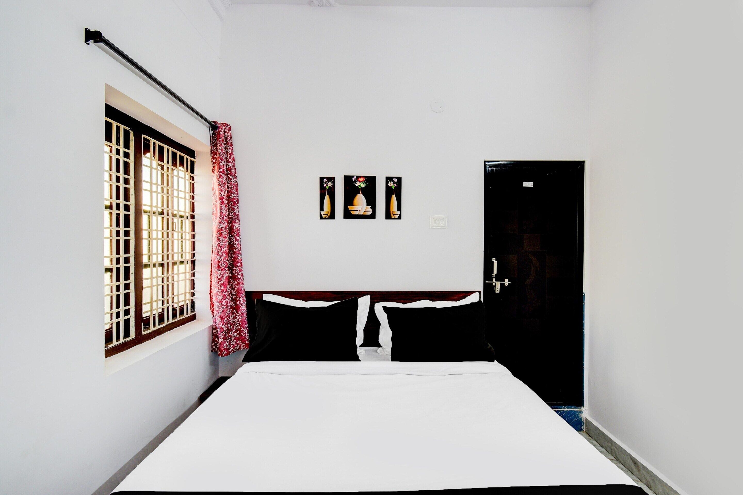 A room with a bed, a window with a metal grille, a door, and three framed pictures on the wall.