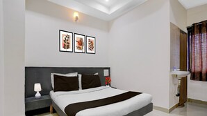 Habitación de hotel con cama, mesita de noche, lámpara, decoración en la pared y baño con lavamanos y cortina de ducha.