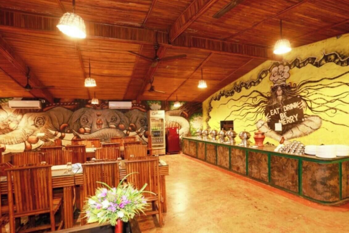 A restaurant interior with wooden ceiling beams, a mural with a chef, and a counter with a sign that says 'EAT DRINK BE Merry'.