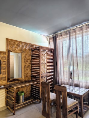 A room with a wooden bench, a table, a mirror, and a window with curtains. - Corbett Soho Resort (Kaladhungi)