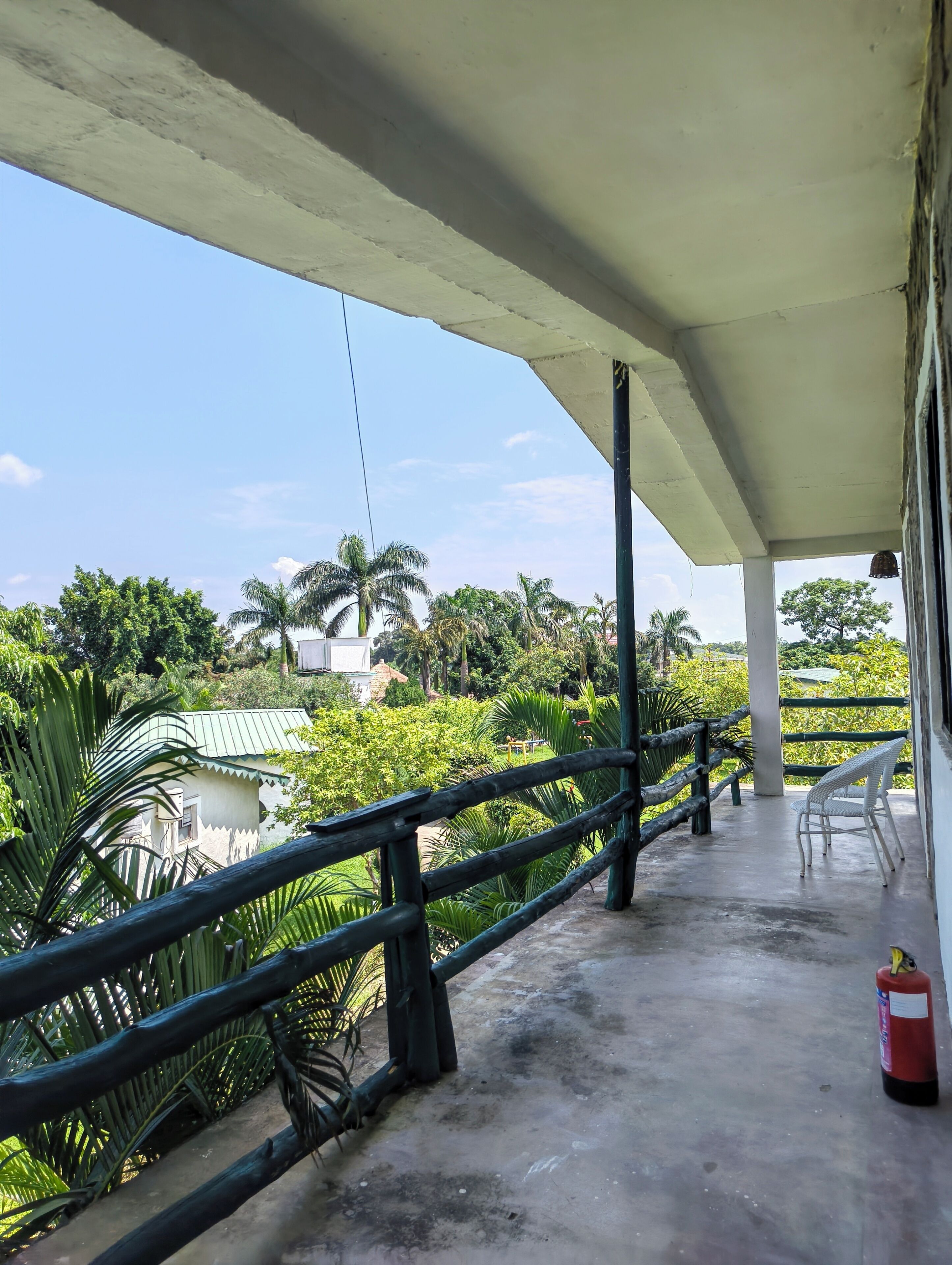 A covered outdoor area with a concrete floor, a metal railing, and a view of greenery and buildings in the distance.