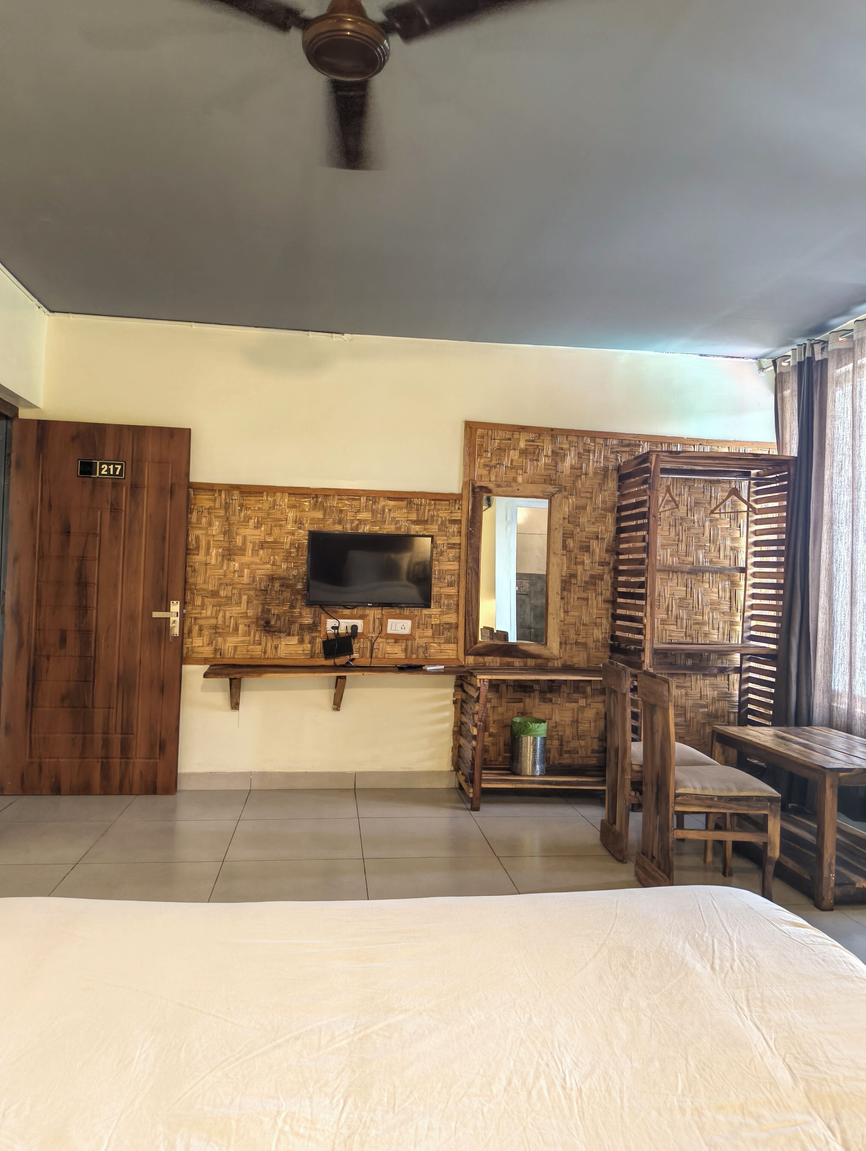 Una habitación con una cama, un televisor fijado en una pared de madera, un espejo y un ventilador de techo.