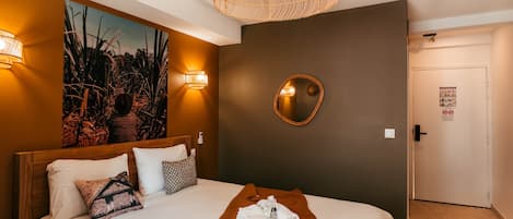Habitación de hotel con cama, espejo en la pared, un cuadro y una puerta con un cartel.