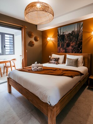 A modern bedroom with a wooden bed, a rattan ceiling light, a wall-mounted lamp, and a large painting. - Héritage Apartment - L'Escale Bleue Saint-Leu, Réunion (Saint-Leu)