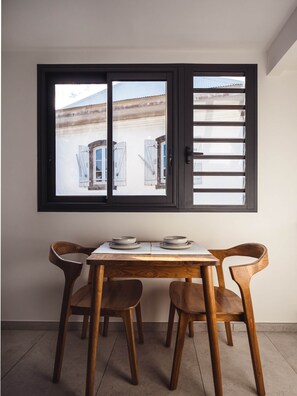 Ein Essbereich mit Tisch und vier Stühlen, ein Fenster mit Jalousien und Blick auf Gebäude im Freien.