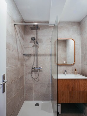 A modern bathroom with a glass-enclosed shower, a wooden vanity, and a mirror with a wooden frame.