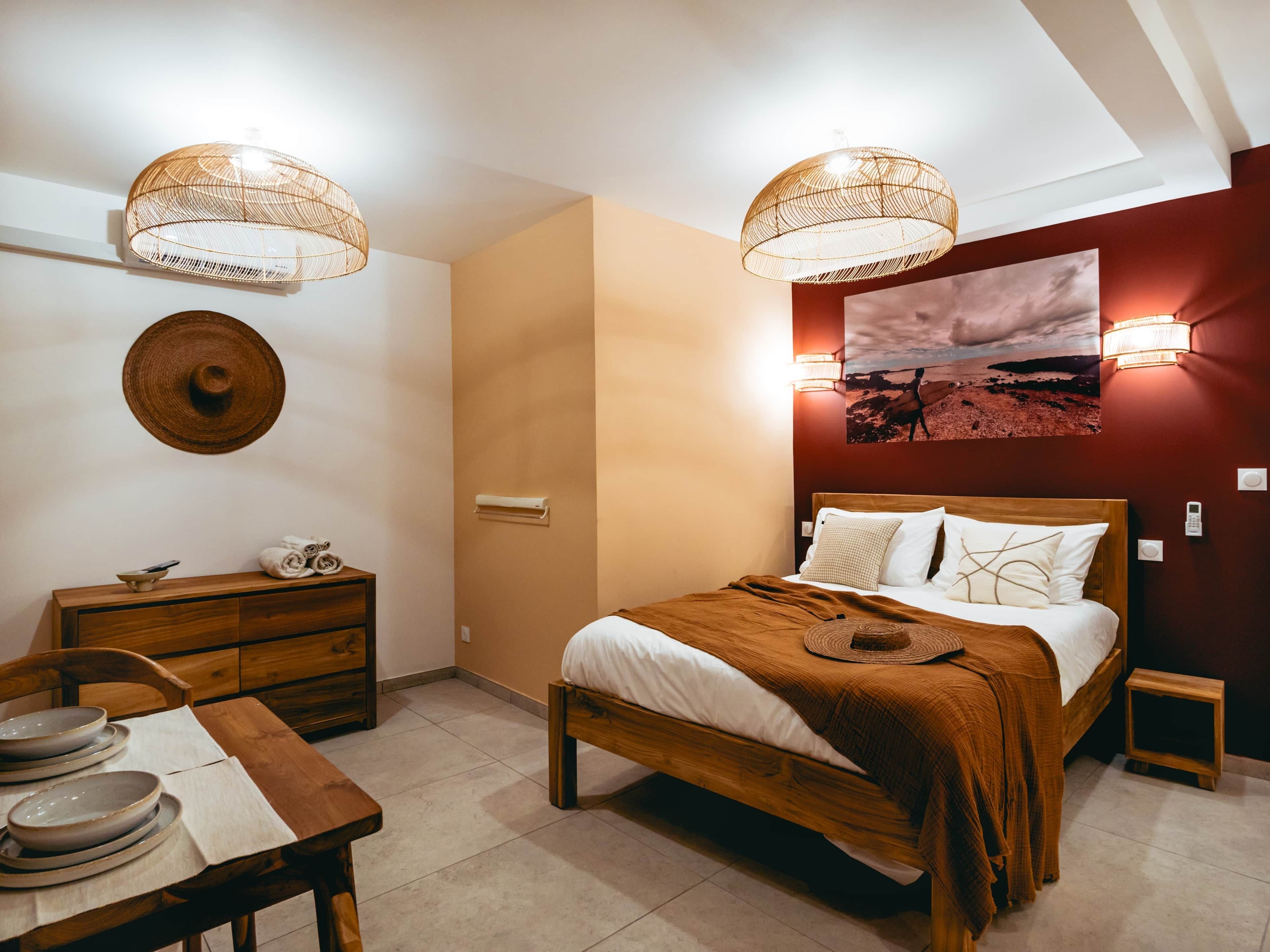 Een slaapkamer met een bed, nachtkastjes, een houten dressoir, een eettafel met borden en een wandlamp.