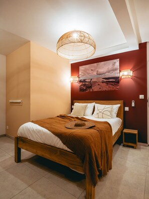A bedroom with a wooden bed, a large wall-mounted picture, and a hanging light fixture. - Pointe au Sel Apartment - L'Escale Bleue, Saint-Leu, Réunion (Saint-Leu)