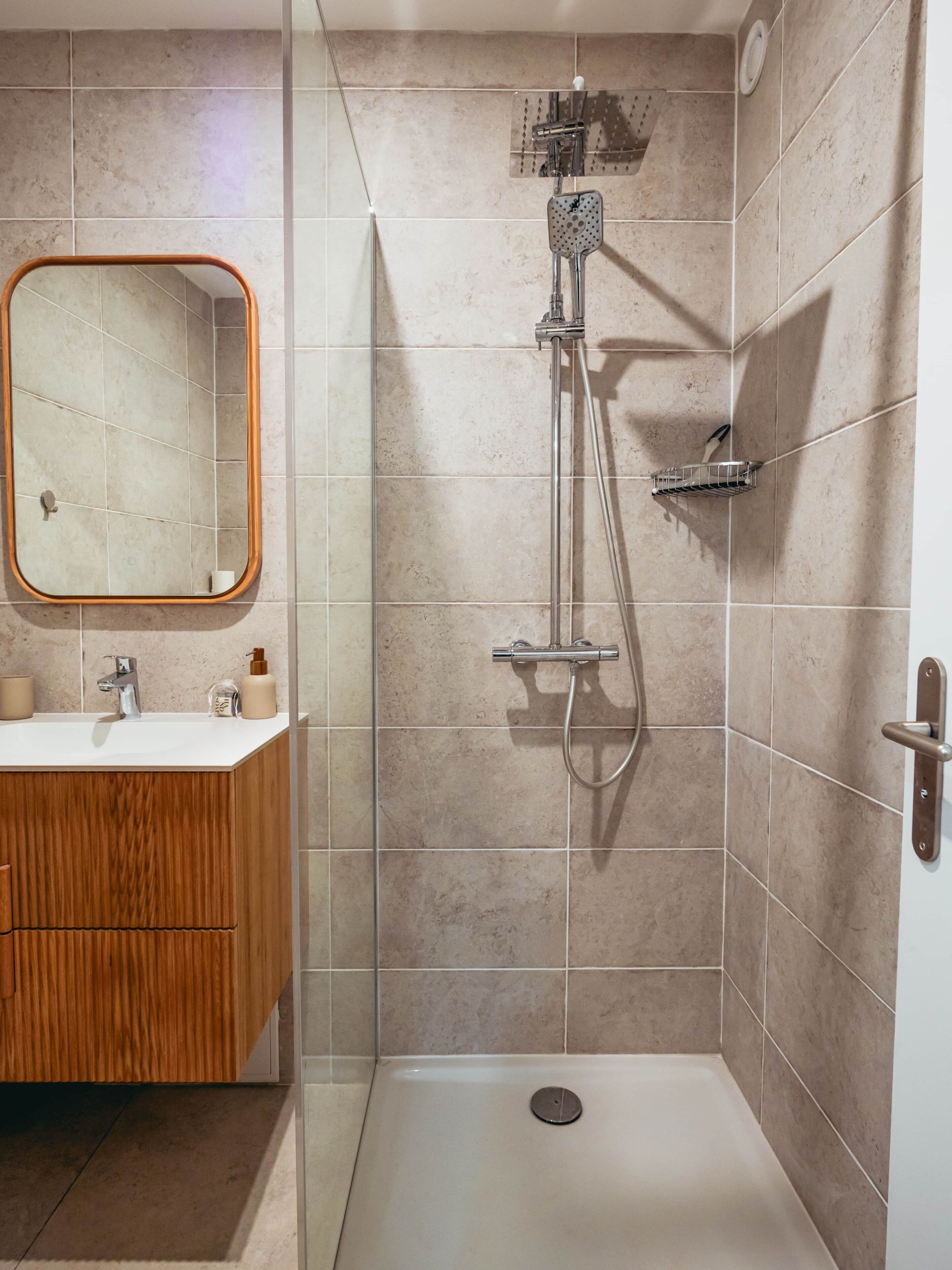 A bathroom with a shower, a sink, a mirror, and a wooden cabinet.