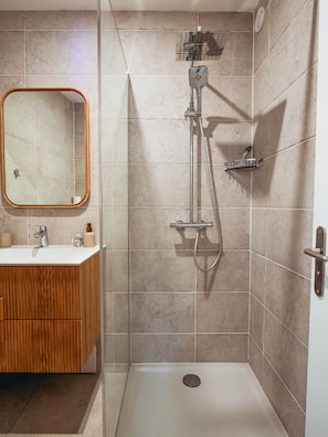 A bathroom with a shower, a sink, a mirror, and a wooden cabinet. - Pointe au Sel Apartment - L'Escale Bleue, Saint-Leu, Réunion (Saint-Leu)